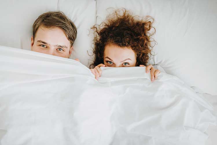 Ein Pärchen im Bett, halb unter der Decke. ACTICORE kann bei Problemen mit der Sexualität helfen